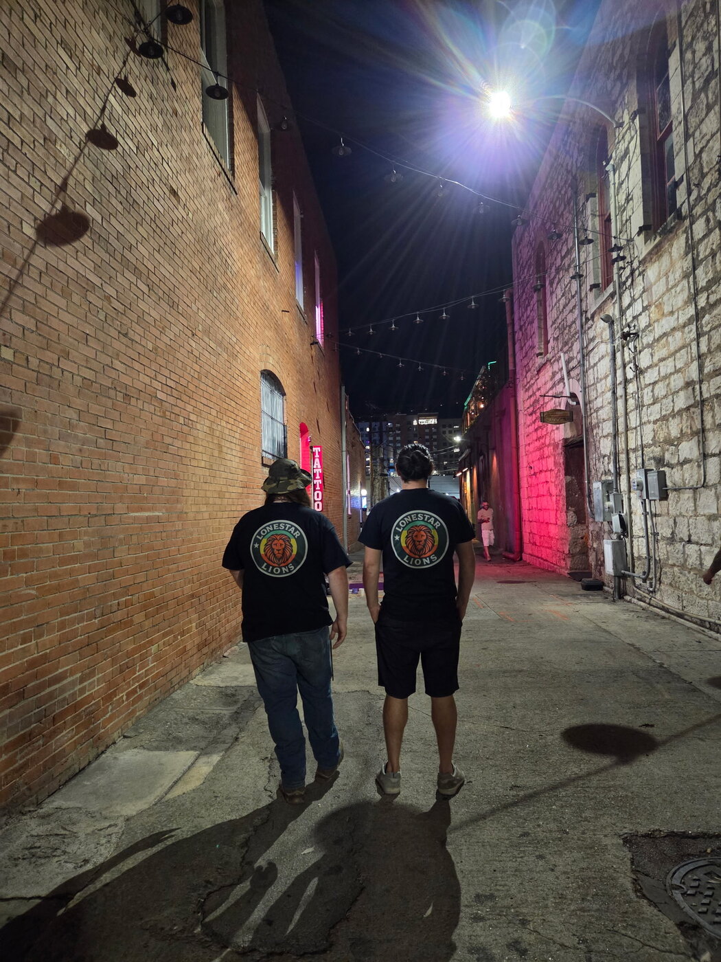 Two people wearing Lonestar Lions shirts in an alley at night